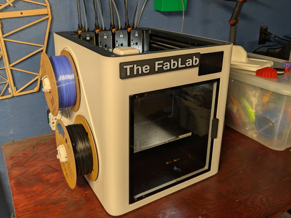 A 3D printer labelled The FabLab on a workbench, with spools of filament