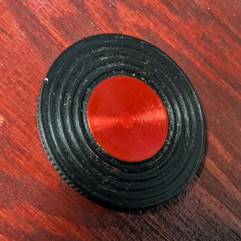 A black 3D printed StillPoint coin on a wooden table, with rippled rings circling out from a red touchstone in the centre
